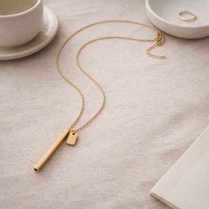 Gold stainless steel breathing necklace styled on a neutral beige surface with ceramic details in a minimal, premium setting
