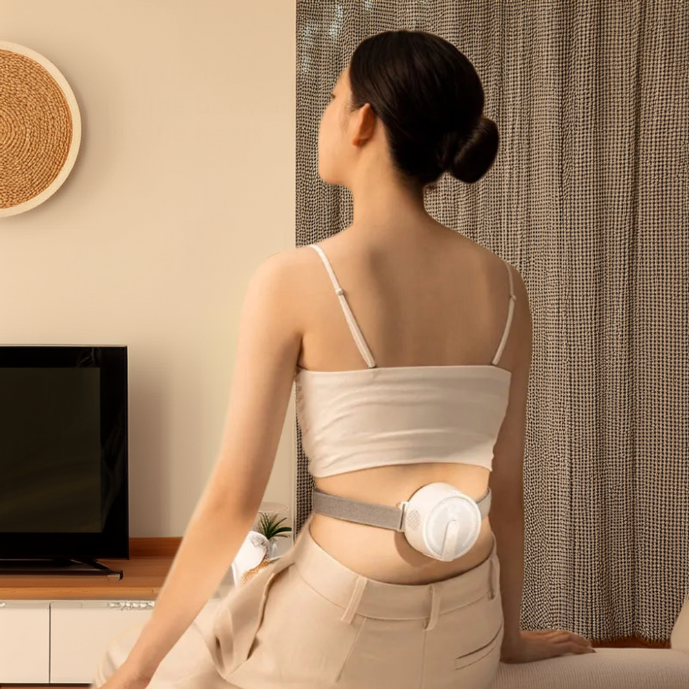 Woman wearing a portable heat therapy device on her lower back while sitting in a living room setting