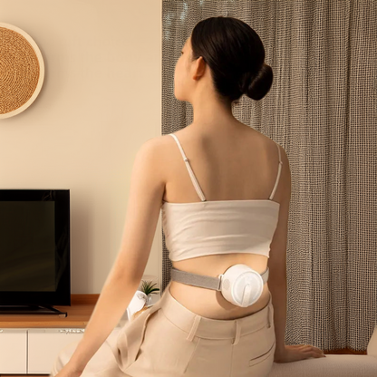 Woman wearing a portable heat therapy device on her lower back while sitting in a living room setting